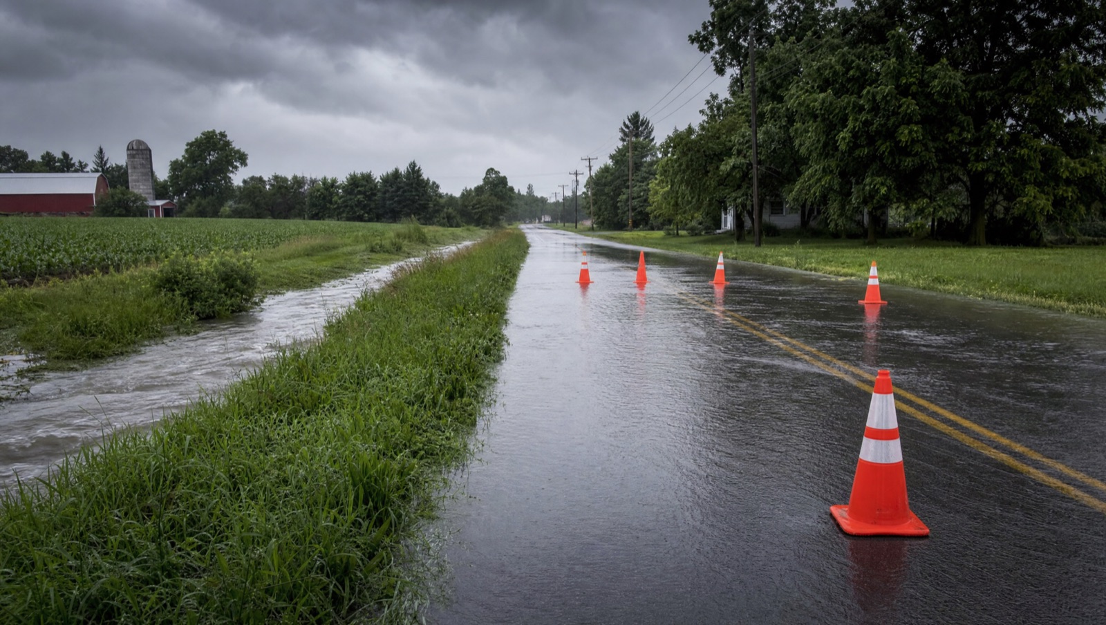Flooded rural county road with standing water and caution cones after a flash flood